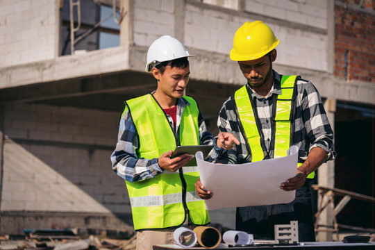 Two Young Asian Construction Workers Reviewing Blueprints on Bui