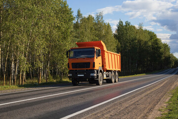 Orange dump truck on a forest road. Construction equipment driving on the highway. © yaviki