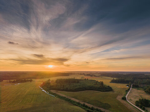 Sunset paints golden sky over rolling green fields and winding paths. Warm light bathes landscape in peaceful, serene glow. Ideal for nature, travel, or countryside-themed projects
