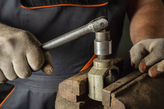 A skilled worker is using a ratchet wrench to tighten a metal component in a busy workshop. The atmosphere is filled with tools and materials, showcasing dedication and hard work