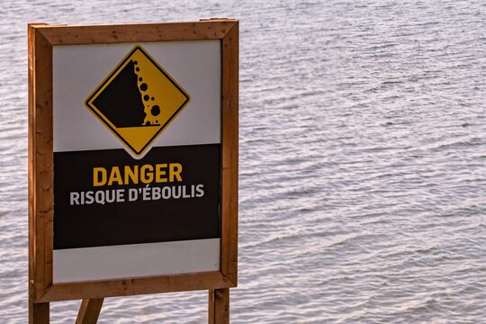 A wooden framed warning sign alerting danger of falling rocks stands in front of rippling water