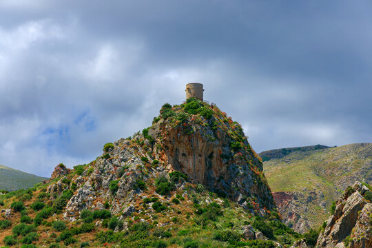 Ancient stone watchtower perched atop a rugged rocky outcrop under moody skies