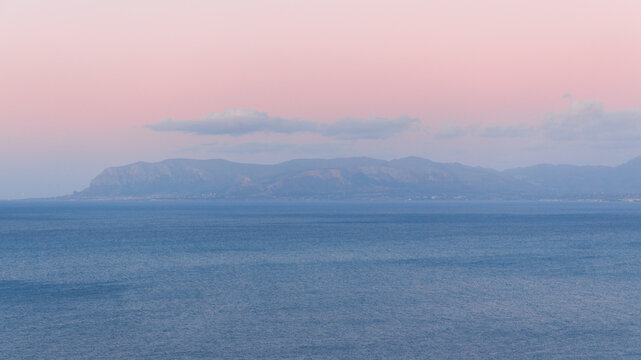 Serene pastel sky over calm blue sea and distant hazy mountains at horizon