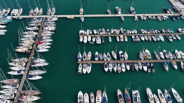 Top down aerial view of Gouvia Marina harbour with boats moored along wooden piers, promenade and parking area in Corfu, Greece