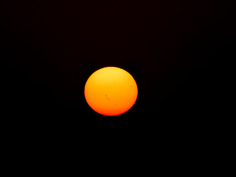 Glowing orange sun disc isolated against a deep black dark sky during sunset or sunrise