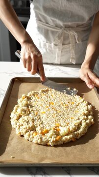 A young female adult in an apron shapes a raw cauliflower pizza crust on a parchment lined baking sheet.