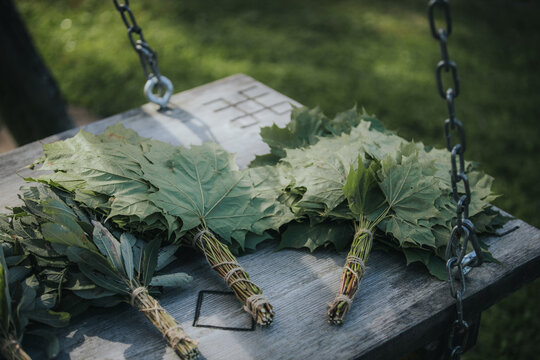 Bundles of fresh green leaves tied with twine resting on a wooden table in a natural outdoor setting with grass and a swing in the background