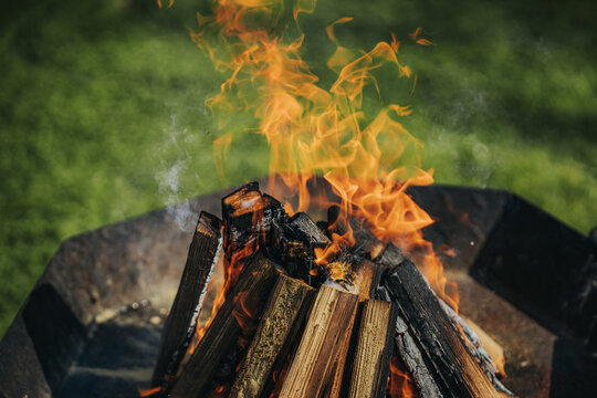 Campfire with bright flames consuming stacked logs in a metal fire pit, surrounded by green grass in a natural outdoor setting