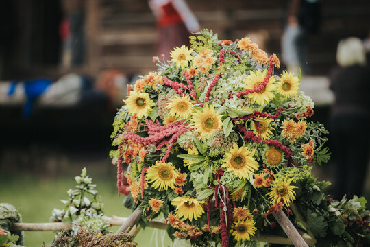 Colorful floral arrangement featuring sunflowers, greenery, and red amaranth displayed outdoors near a rustic wooden structure in a natural setting