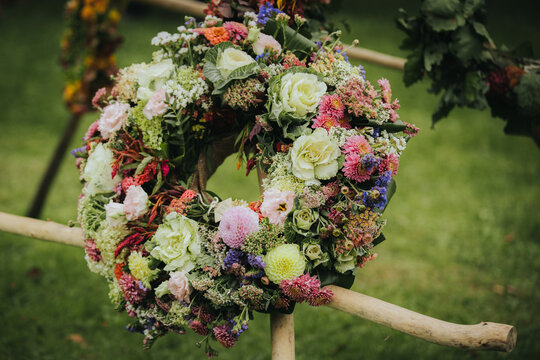 Floral wreath made of various colorful flowers including roses, chrysanthemums, and greenery displayed on a wooden stand in a garden setting