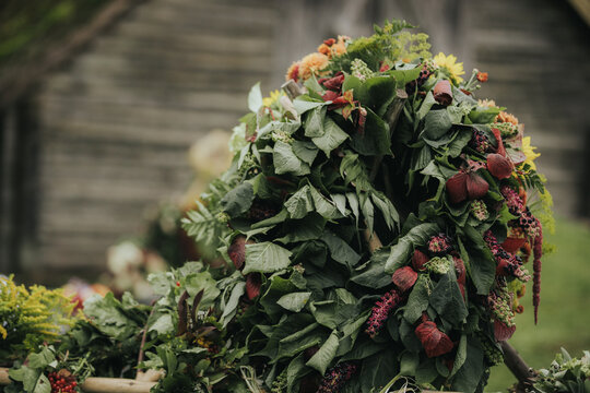 Decorative floral wreath made of various green leaves, berries, and flowers displayed outdoors against a rustic wooden background