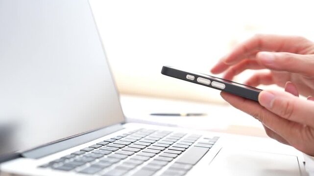 Business employee typing on laptop keyboard while holding smartphone, digital technology workplace with multitasking, online work, professional communication, productivity and modern office workflow.