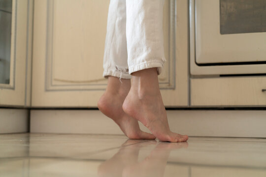 Person stands on heated floor in kitchen, feeling warmth on bare feet during morning routine in home environment