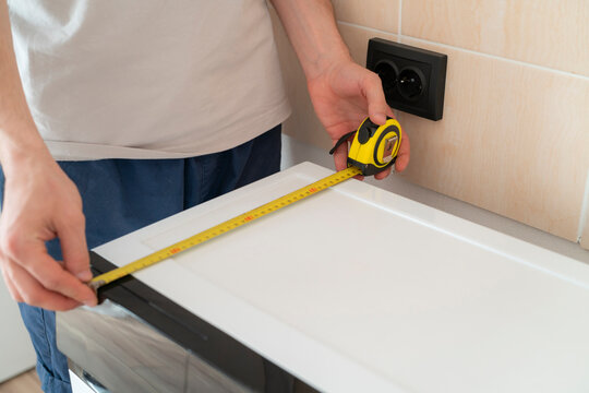 A person is using a tape measure to check the size of a countertop near an electrical outlet in a kitchen