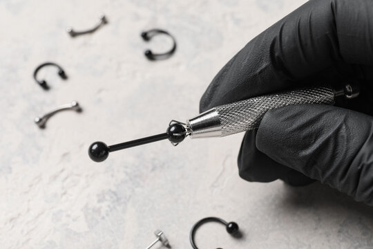 Body piercing and professional modification, piercer holding jewelry with tool for safe procedure in studio