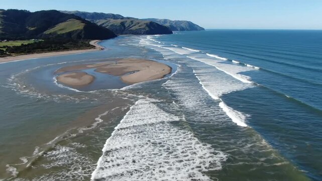 Coastal aerial view of turquoise ocean waves crashing on the shore with lush green mountains and a clear blue sky