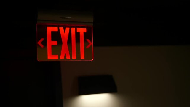 Illuminated red exit sign with directional arrows in a dimly lit interior space