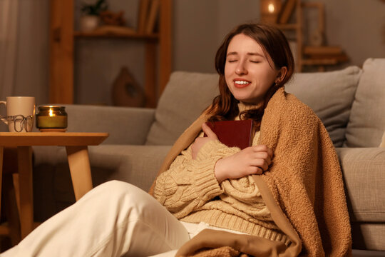 Self care and mindfulness, woman relaxing at home with a book and blanket in cozy evening atmosphere