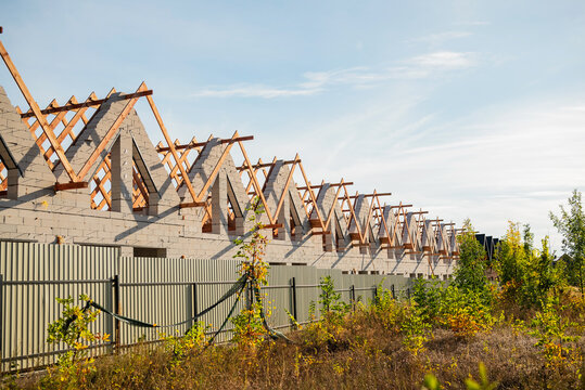 Unfinished residential building with exposed wooden roof trusses and concrete block walls under a blue sky