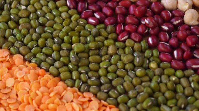 Lentils and beans form colorful ingredient pattern, with orange split lentils, green mung beans, red beans, and chickpeas arranged in diagonal bands across market style food display.