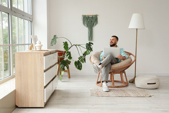 Handsome man using laptop in cocoon chair at home