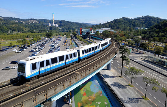 A metro train traveling on the elevated rail over a parking lot, arriving at Mucha Zoo Station of Taipei MRT System in the suburban area of Mucha, Taipei, under blue clear sky on a beautiful sunny day