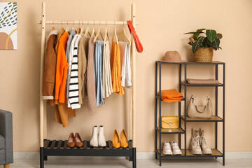 Rack with clothes and shelving unit near beige wall in dressing room