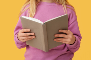 Obraz premium Little girl with book on yellow background
