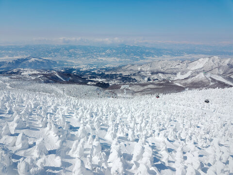 A scenic cable car flying over a forest of Juhyo (ice trees or snow monsters) on the slope & distant mountains covered with snow on a sunny winter day in Zao hot spring & ski resort in Yamagata, Japan