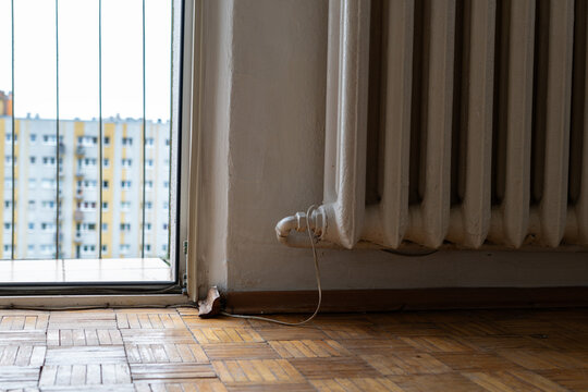 Old apartment interior with worn parquet floor, outdated radiator and window, residential room requiring renovation and repair