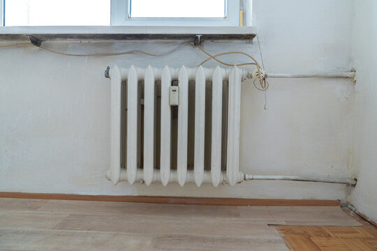 Old apartment interior with outdated cast iron radiator, exposed wiring and mismatched flooring, poor home condition requiring renovation and refurbishment