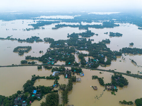 11 July 2026: Aerial view of a flooded landscape with houses and trees partially submerged in murky floodwaters under an overcast sky.