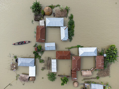 06 July 2024: Aerial view of a flooded village with houses featuring metal roofs surrounded by rising floodwaters and a small boat navigating the area.