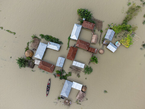 06 July 2024: Aerial view of flooded rural houses surrounded by murky floodwaters with a small wooden boat navigating between buildings.