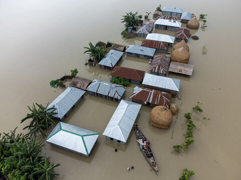 06 July 2024: Aerial view of a village submerged by floodwaters, with houses surrounded by water, a small boat with people, and thatched haystacks visible.