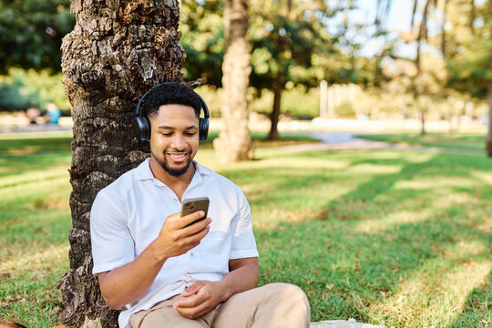 Young man enjoys sunny day while using smartphone and listening to music with earphones in urban setting, highlighting his joy and connection to the world around him