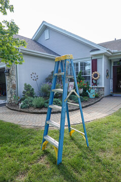 Blue and yellow ladder on the grass in front of a house