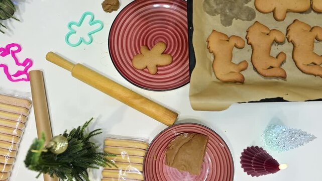 In a cozy kitchen, a woman's hands gently lift freshly baked gingerbread cookies from a warm baking sheet onto a charming plate. Christmas decorations twinkle in the background.