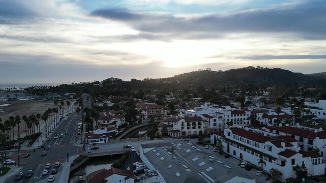 Aerial moving forward following Cabrillo Blvd. on a rainy dusk early evening in Santa Barbara, California, over palm trees and classic Spanish architecture. 