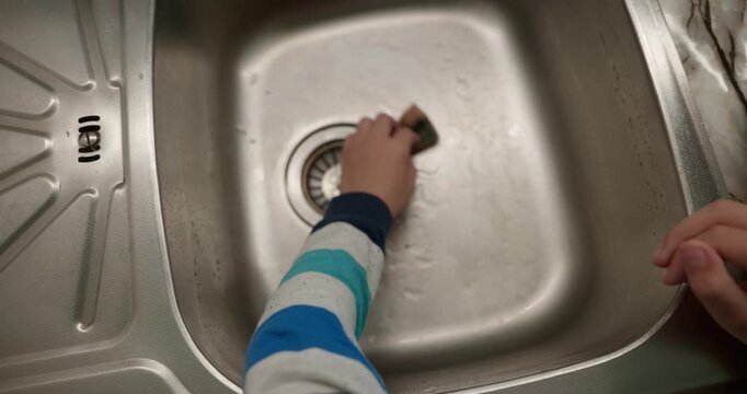 Close-up children's hands wash kitchen utensils sink and dishes. 4K 10-bit