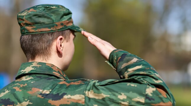 Side view of soldier in camouflage uniform saluting outdoors
