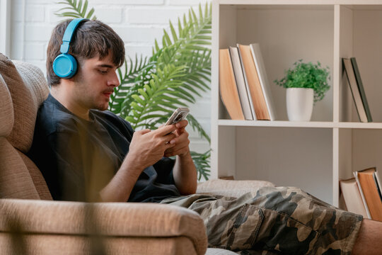 Young man wearing headphones and using a smartphone while relaxing at home