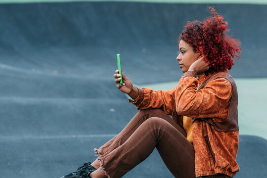 Young mixed-race woman sitting outdoors taking a selfie photo with her smartphone, side profile view, confident urban lifestyle portrait