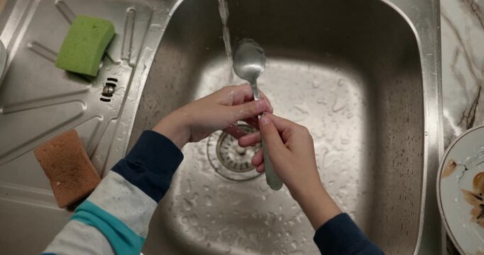 Close-up children's hands wash kitchen utensils sink and dishes. 4K 10-bit