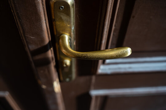 Worn metal lever handle and rectangular backplate on a paneled wooden door, illustrating frequently used entrance hardware and traditional mechanical door operation