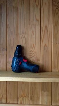 Camera panning to right across wooden workshop wall with cordless drill on shelf