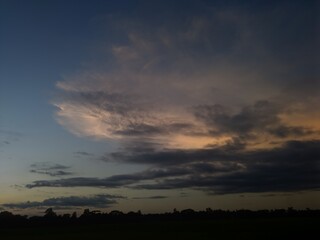 Obraz premium Moody evening cloudscape displaying soft golden sunset hues in dark sky