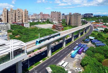 Fototapeta premium Aerial view of a metro train traveling on a railway curve and arriving at a station of Danhai Light Rail with residential towers under sunny sky in background in Tamsui District, New Taipei City