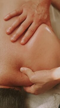 two hands massage oiled shoulder and upper back with gentle pressure promoting relaxation in spa calm scene