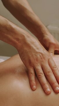 closeup view of two hands pressing and gliding over oiled bare upper back during therapeutic massage in clinic